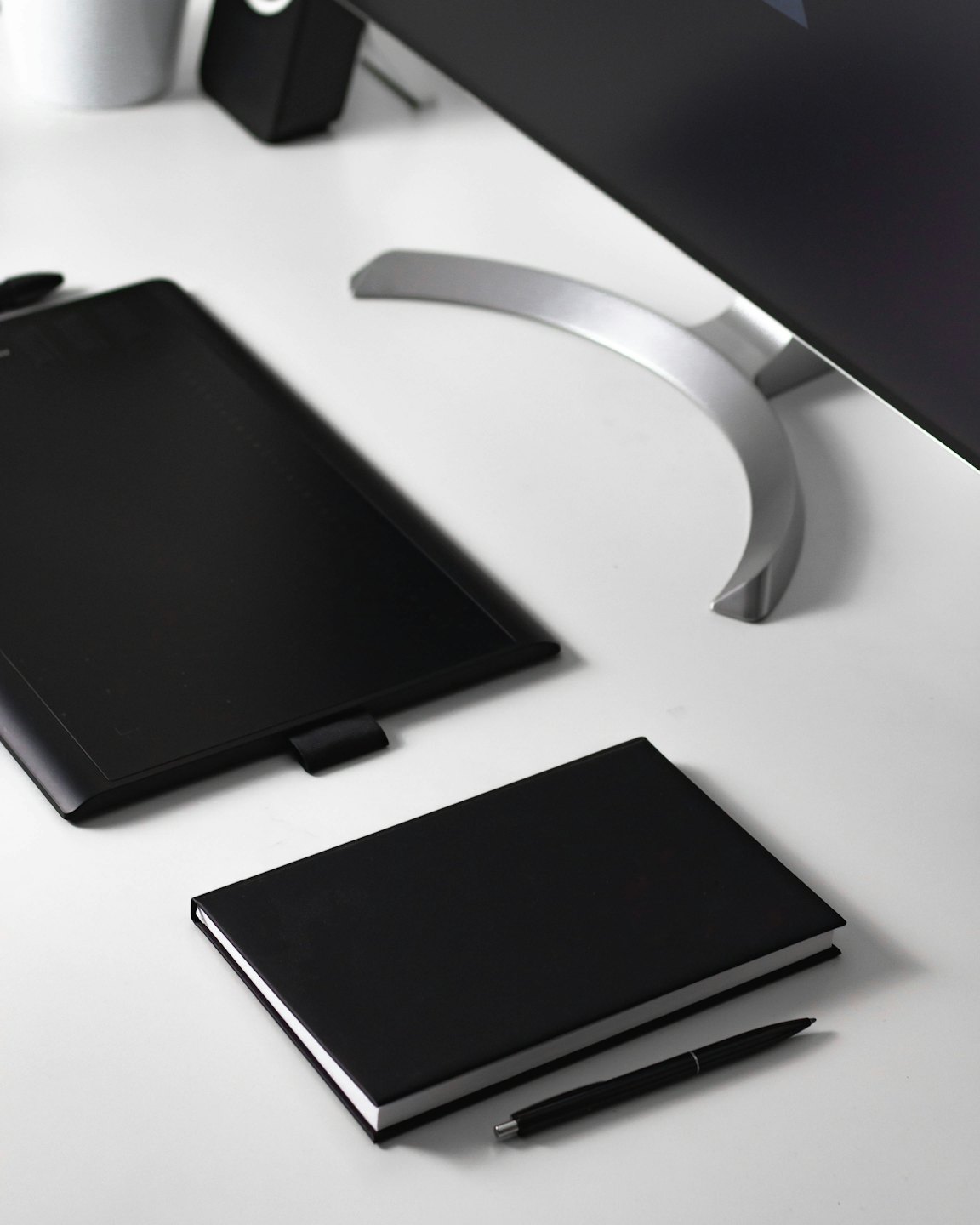 Black graphic tablet, notebook, and pen on a white desk.